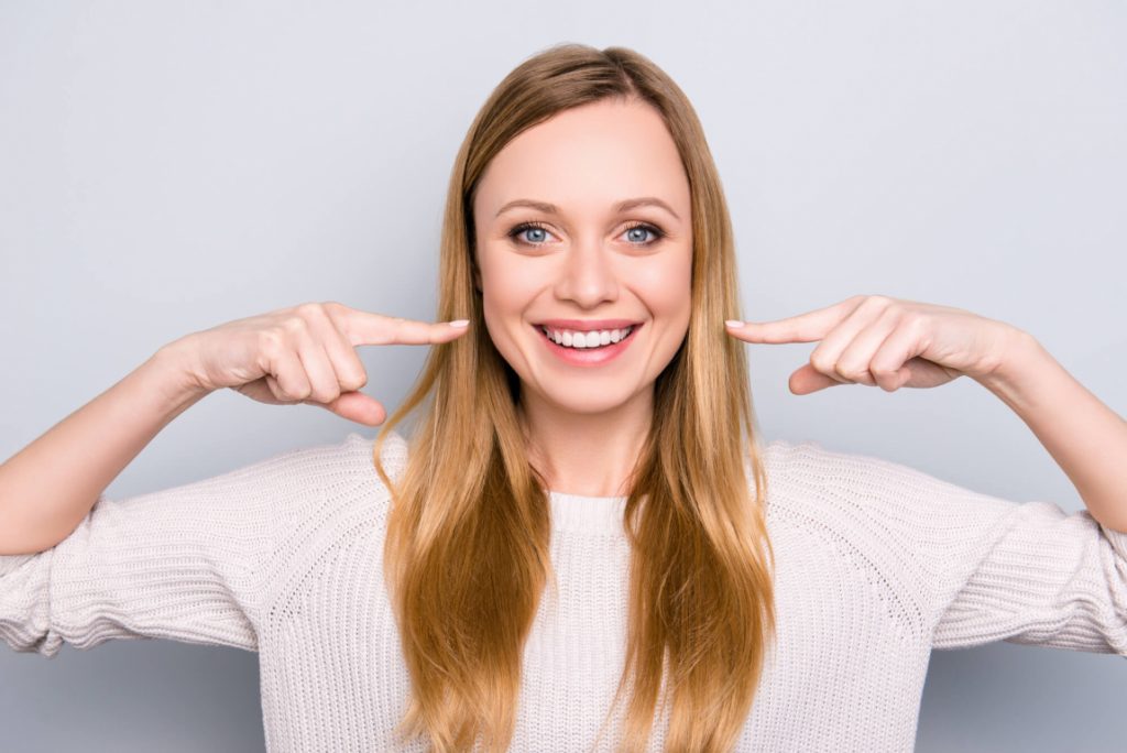 woman points at her teeth with porcelain veneers in Medford
