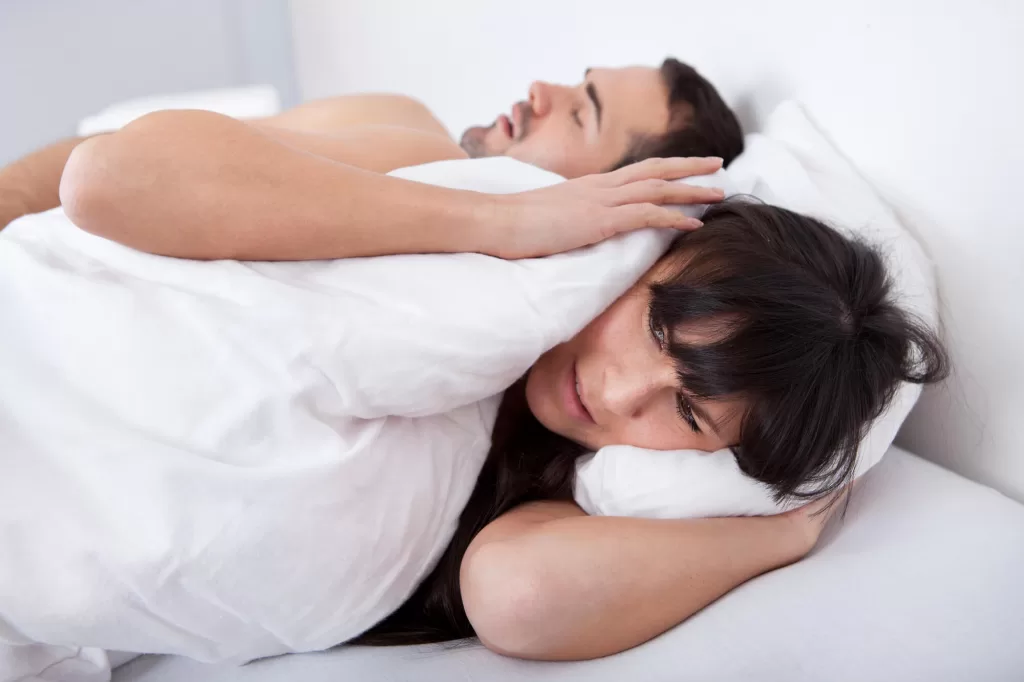Man snoring due to phillips sleep apnea while partner cover her ears