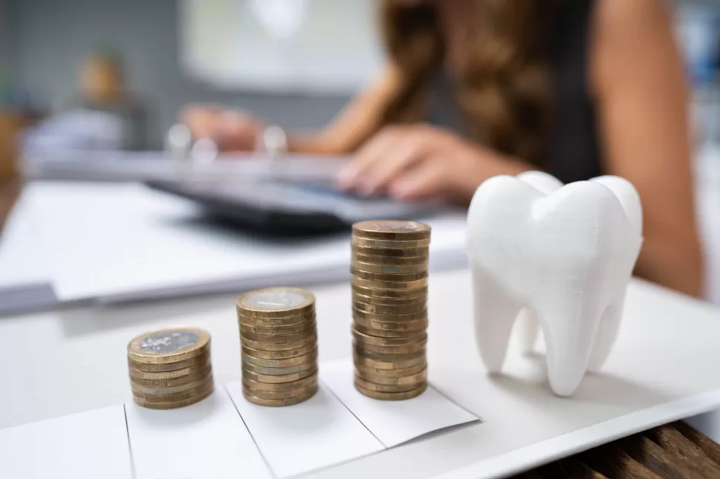 close up of coins next to the model of a tooth at a dental office as concept for affordable dental in medford